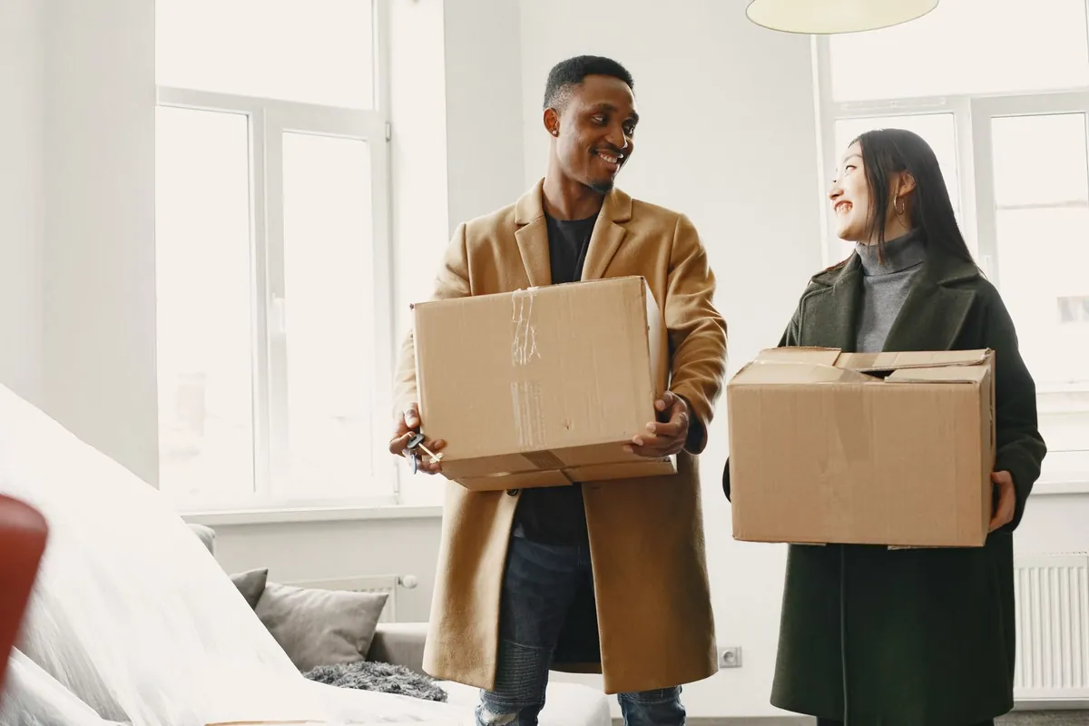 A couple carrying moving boxes into a bright apartment